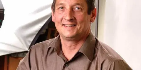 Portrait of a male photographer holding a camera in a studio.