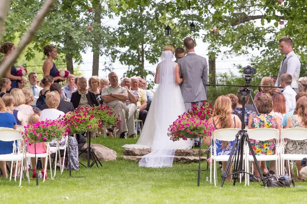 Outdoor wedding ceremony with bride and groom at an altar surrounded by seated guests and floral arrangements.