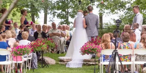 Outdoor wedding ceremony with bride and groom at an altar surrounded by seated guests and floral arrangements.
