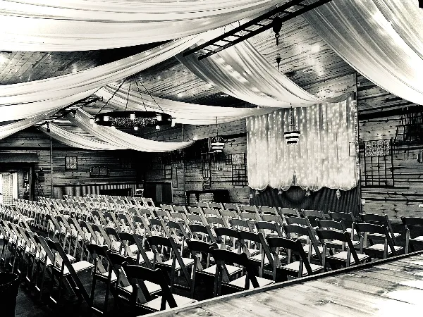 Interior of a rustic wooden wedding venue with rows of chairs and draped ceiling fabric.