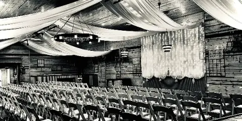Interior of a rustic wooden wedding venue with rows of chairs and draped ceiling fabric.