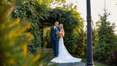 A bride and groom standing together under a green archway in a garden setting.