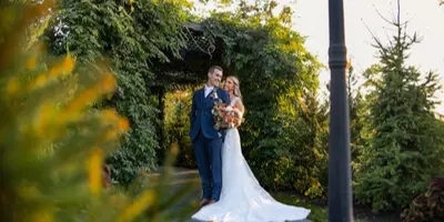 A bride and groom standing together under a green archway in a garden setting.