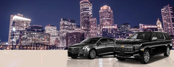 A black luxury sedan and a black SUV parked in front of the Boston city skyline at night.