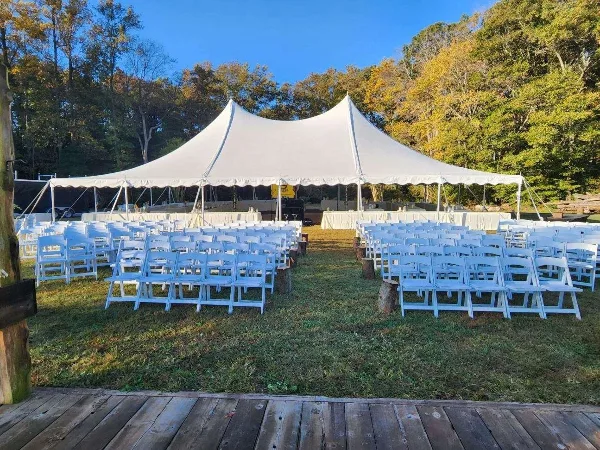 Outdoor wedding setup featuring a large white tent, rows of white folding chairs, and tables on a grassy lawn.