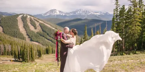 A bride and groom kissing in a mountainous outdoor setting with a flowing white dress and bouquet.