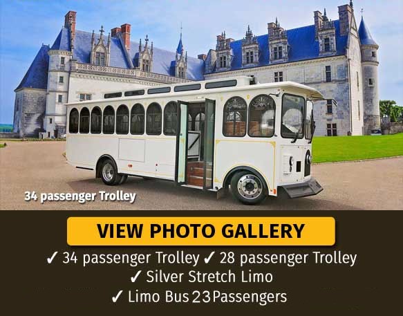 A white 34-passenger wedding trolley parked in front of a large castle-style building.