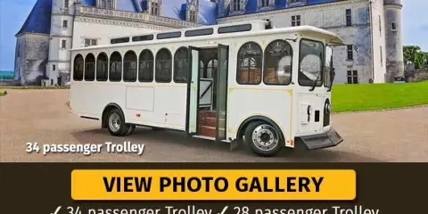 A white 34-passenger wedding trolley parked in front of a large castle-style building.