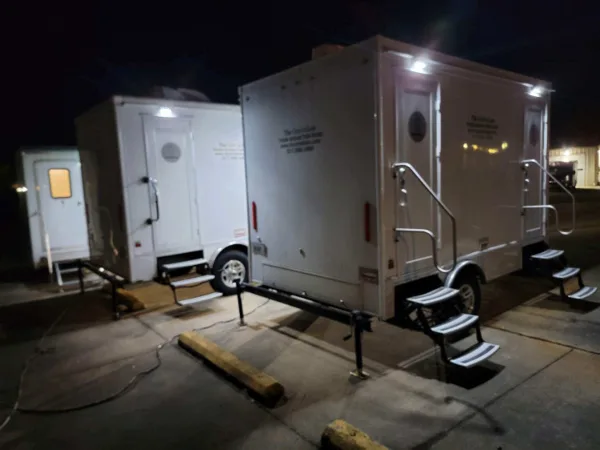 White portable restroom trailers with steps and exterior lighting parked at night.