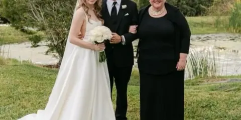 A bride and groom standing with their officiant outdoors after a wedding ceremony.