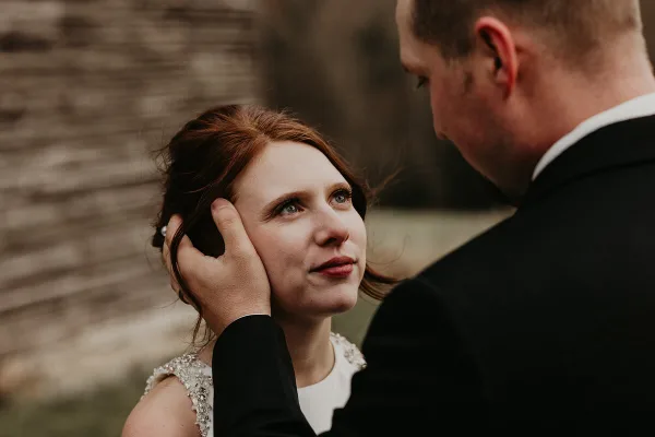 A candid close-up photograph of a bride and groom sharing an intimate moment outdoors.