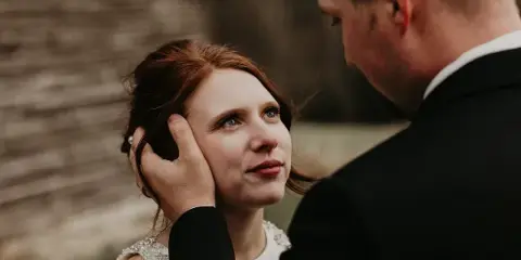 A candid close-up photograph of a bride and groom sharing an intimate moment outdoors.