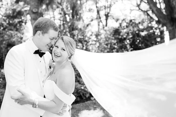 A black and white photograph of a bride and groom smiling and embracing outdoors.