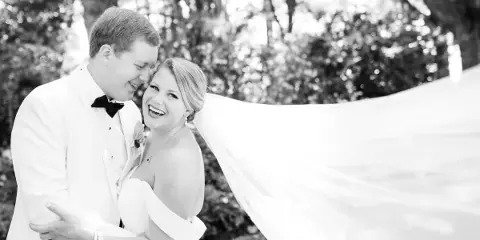 A black and white photograph of a bride and groom smiling and embracing outdoors.