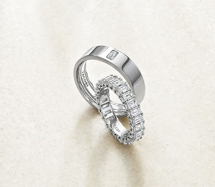 A pair of diamond wedding bands, one plain and one with a channel-set diamond design, resting on a light-colored surface.