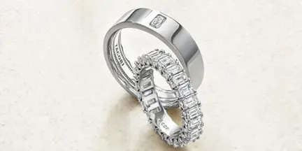 A pair of diamond wedding bands, one plain and one with a channel-set diamond design, resting on a light-colored surface.