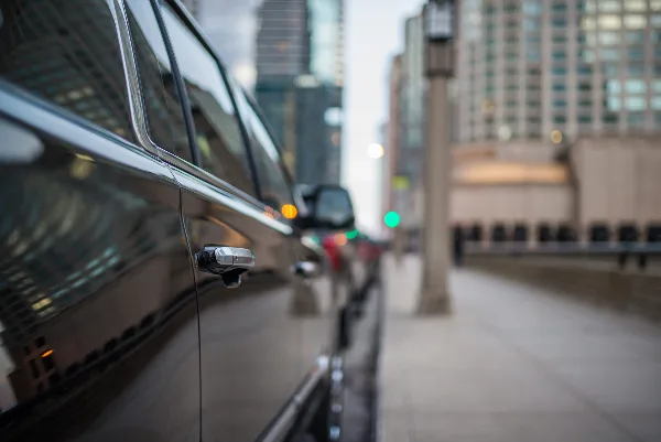 A black luxury car parked on a city street with high-rise buildings in the background.
