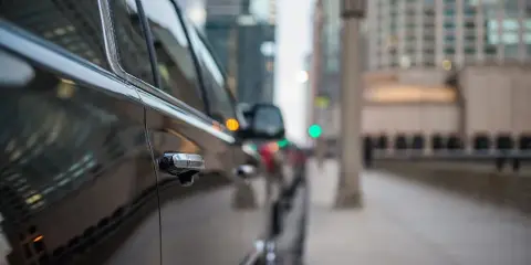 A black luxury car parked on a city street with high-rise buildings in the background.