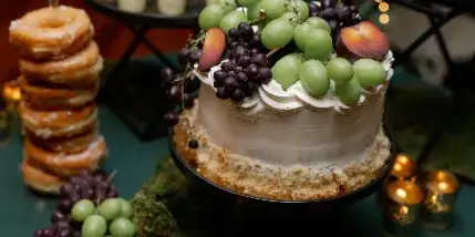 Wedding dessert table with a fruit-topped cake, pastries, desserts, grapes, and candlelight.