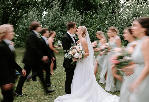 A bride and groom kissing during an outdoor wedding ceremony with their wedding party standing on either side.