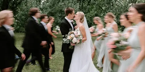 A bride and groom kissing during an outdoor wedding ceremony with their wedding party standing on either side.