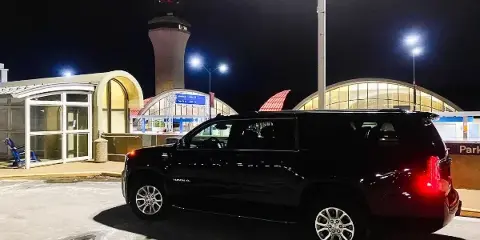 A black luxury SUV parked at an airport terminal at night.