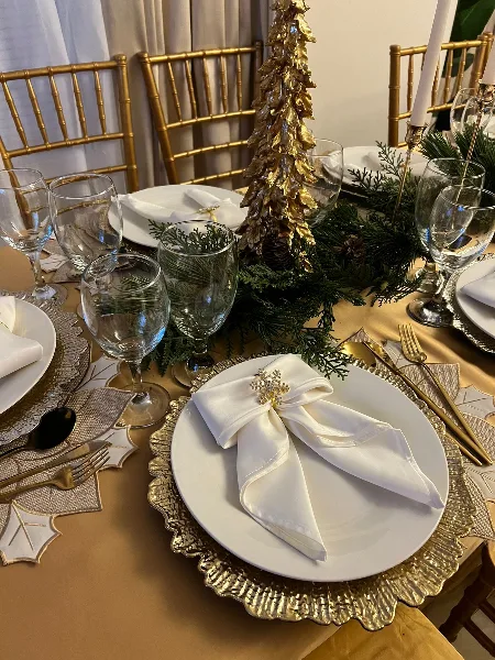 Elegant event table setting with gold charger plates, glassware, and white napkins.