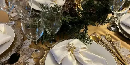 Elegant event table setting with gold charger plates, glassware, and white napkins.