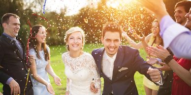 A bride and groom smiling and celebrating with guests at an outdoor wedding event.