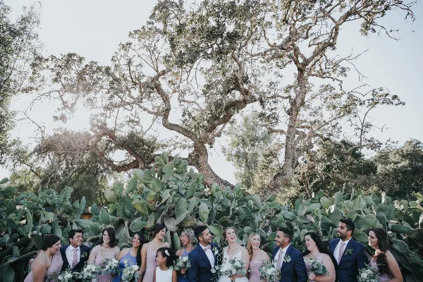 A wedding party posing outdoors with floral bouquets and boutonnieres.
