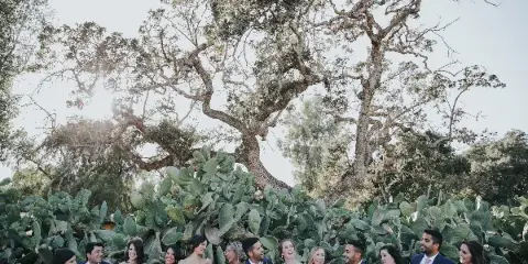 A wedding party posing outdoors with floral bouquets and boutonnieres.