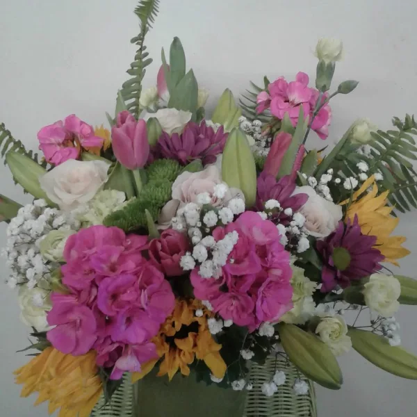 A colorful floral arrangement featuring pink snapdragons, white roses, and yellow sunflowers in a vase.