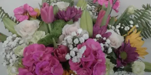 A colorful floral arrangement featuring pink snapdragons, white roses, and yellow sunflowers in a vase.