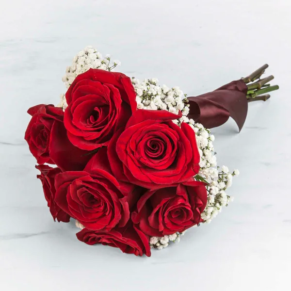 A bouquet of red roses with white baby's breath and a dark ribbon, resting on a white marble surface.