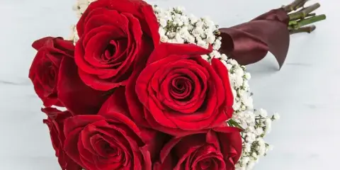 A bouquet of red roses with white baby's breath and a dark ribbon, resting on a white marble surface.