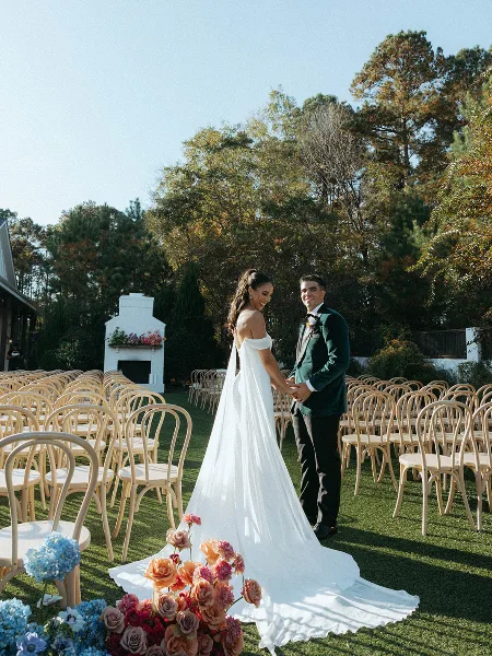 A bride and groom standing in an outdoor wedding ceremony setup with rows of chairs and floral arrangements.