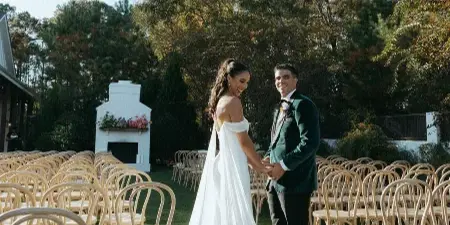 A bride and groom standing in an outdoor wedding ceremony setup with rows of chairs and floral arrangements.