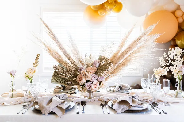 Styled event table with linen, charger plates, flatware, glassware, and a floral centerpiece.