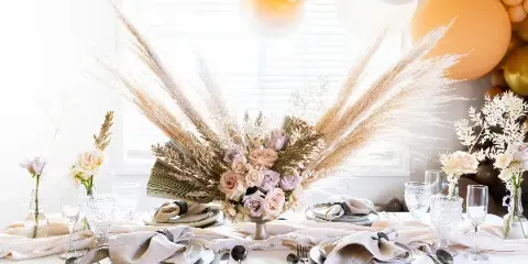 Styled event table with linen, charger plates, flatware, glassware, and a floral centerpiece.