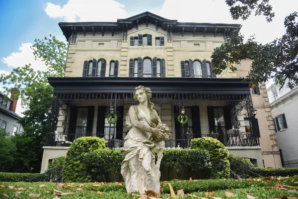 Exterior view of Brockington Hall, a historic building in Savannah, featuring a stone statue in the foreground and a manicured garden.