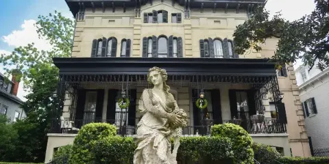 Exterior view of Brockington Hall, a historic building in Savannah, featuring a stone statue in the foreground and a manicured garden.