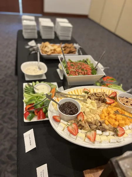 A catering table set with a large cheese and fruit platter, vegetable tray, and salad bowls.