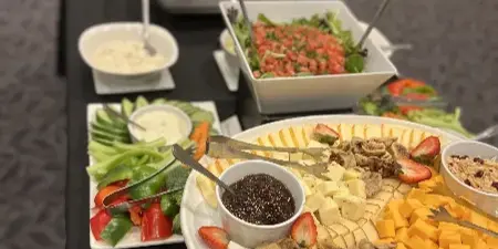 A catering table set with a large cheese and fruit platter, vegetable tray, and salad bowls.