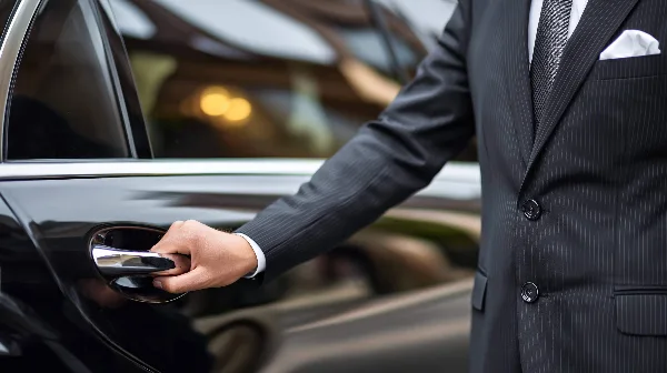 A professional chauffeur in a dark suit opening the door of a black luxury car.