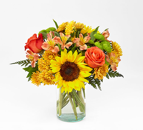 A vase arrangement featuring a large sunflower, orange roses, and yellow chrysanthemums.