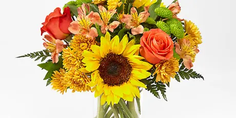 A vase arrangement featuring a large sunflower, orange roses, and yellow chrysanthemums.