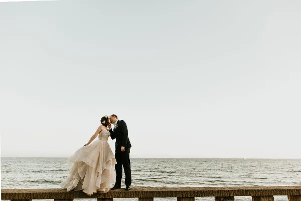 A bride and groom kissing on a stone pier overlooking the ocean.