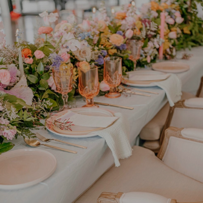 A decorated event table with white linens, floral arrangements, glassware, and plates.