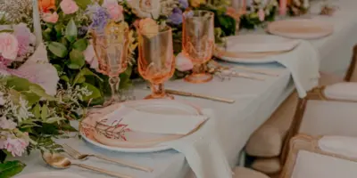 A decorated event table with white linens, floral arrangements, glassware, and plates.