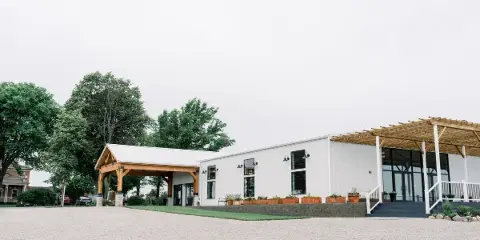 Exterior view of The 1868 Farmhouse wedding venue, showing a white metal building with a wooden pergola and covered entryway.